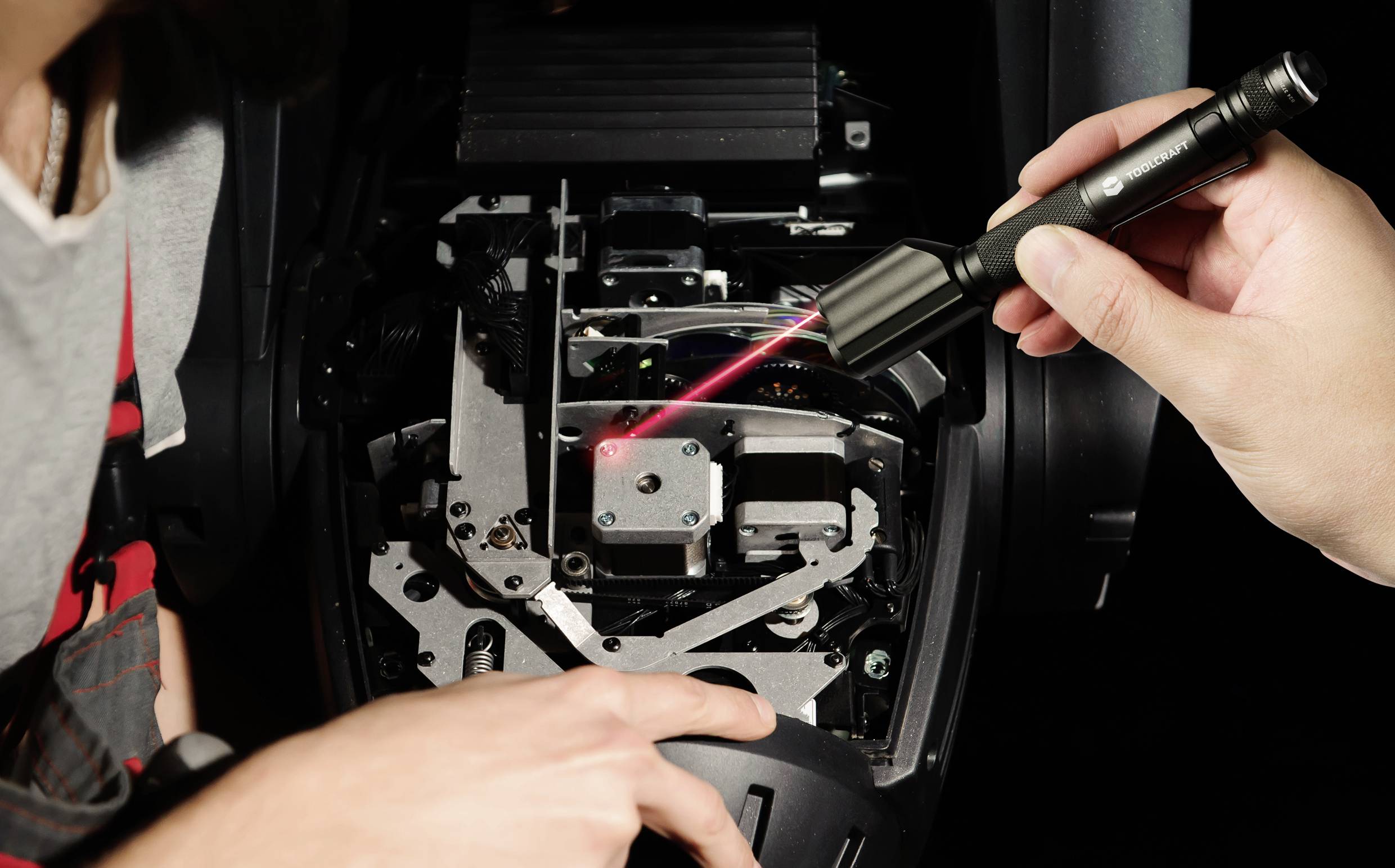 Person zeigt mit Laserlicht auf technische Komponenten in einem geöffneten Gerät, möglicherweise zur Diagnose oder Reparatur.