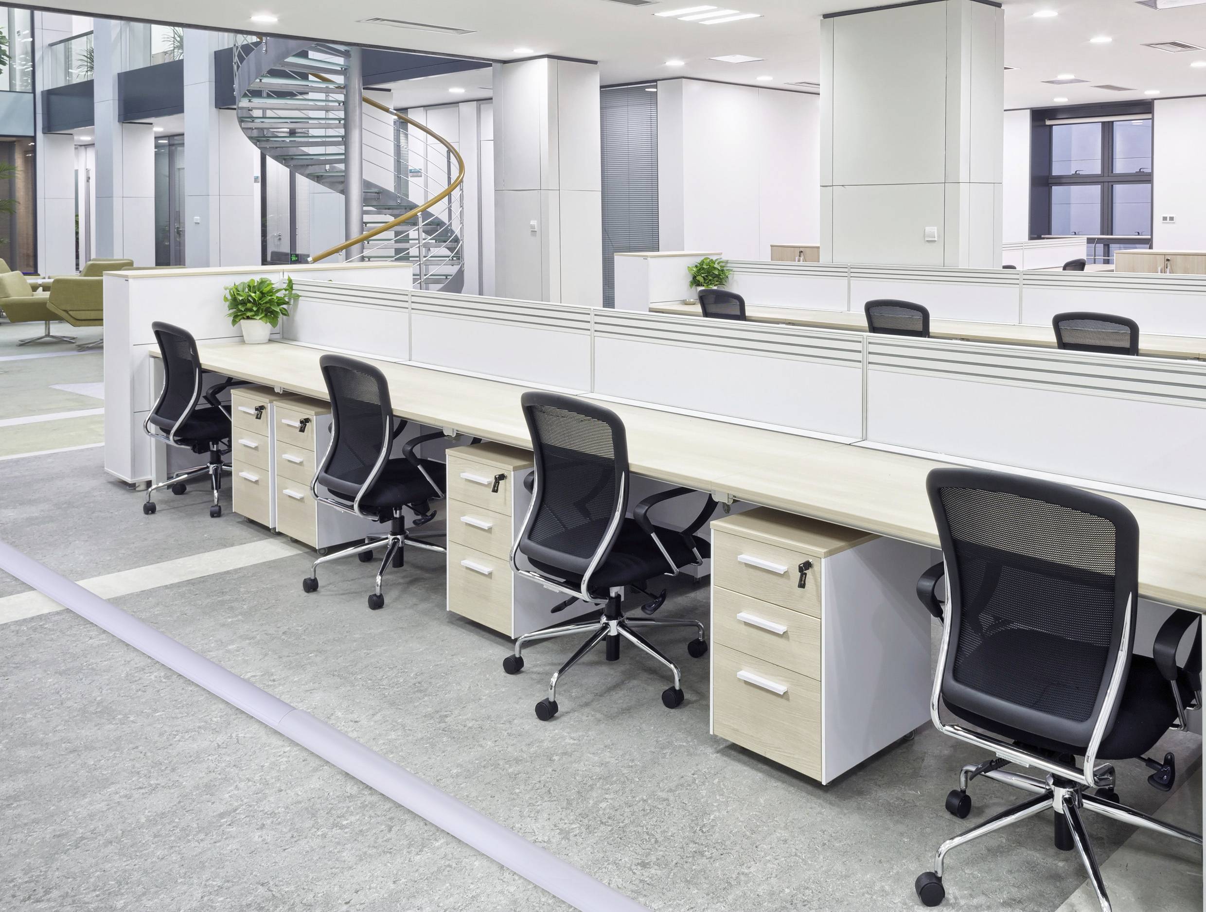 Offenes, modernes Büro mit mehreren Schreibtischen und Drehstühlen. Eine Wendeltreppe und Pflanzen sind im Raum zu sehen.