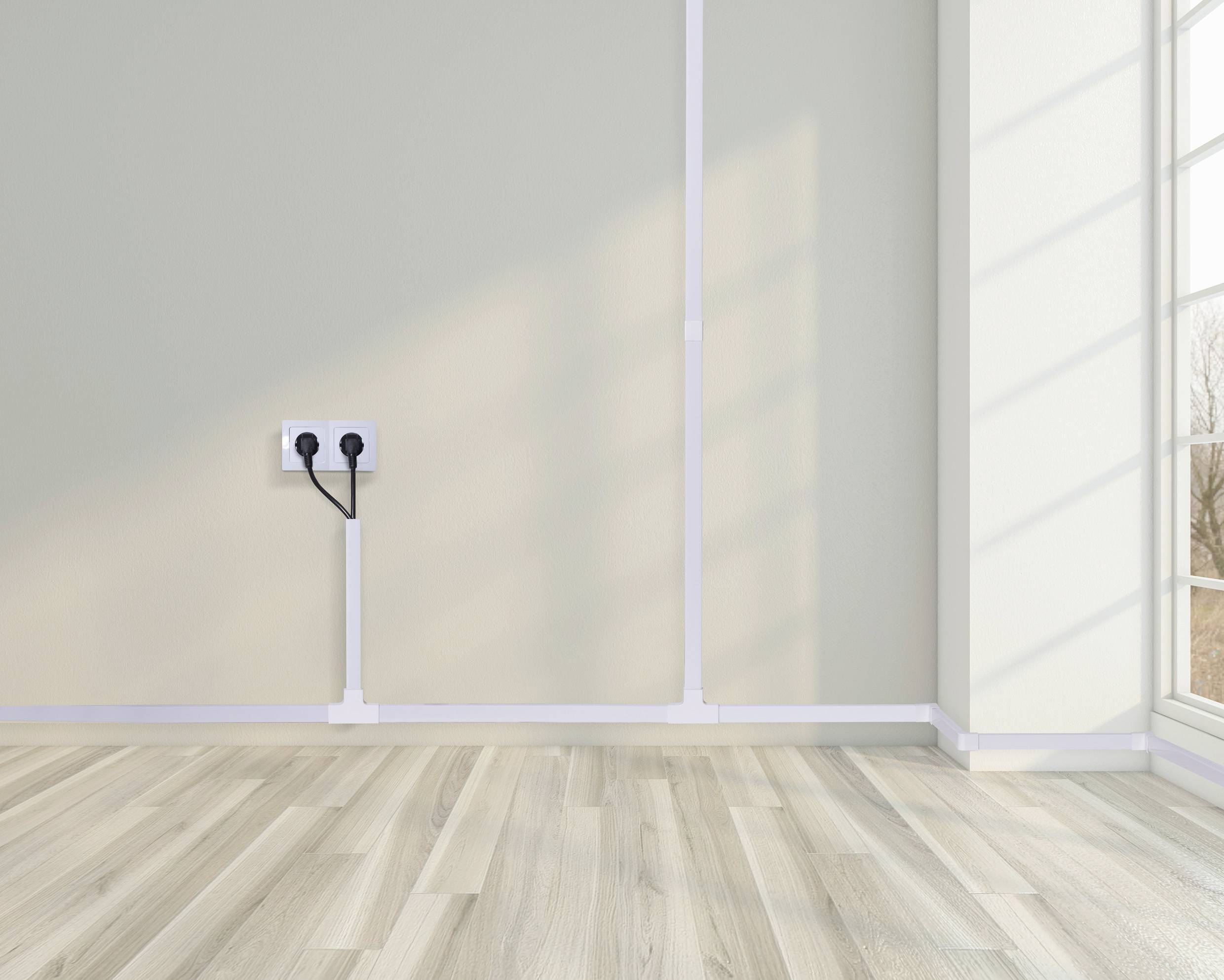 Ein leeres Zimmer mit hellem Holzboden, einer Steckdose mit zwei eingesteckten Kabeln an der Wand und einem großen Fenster.