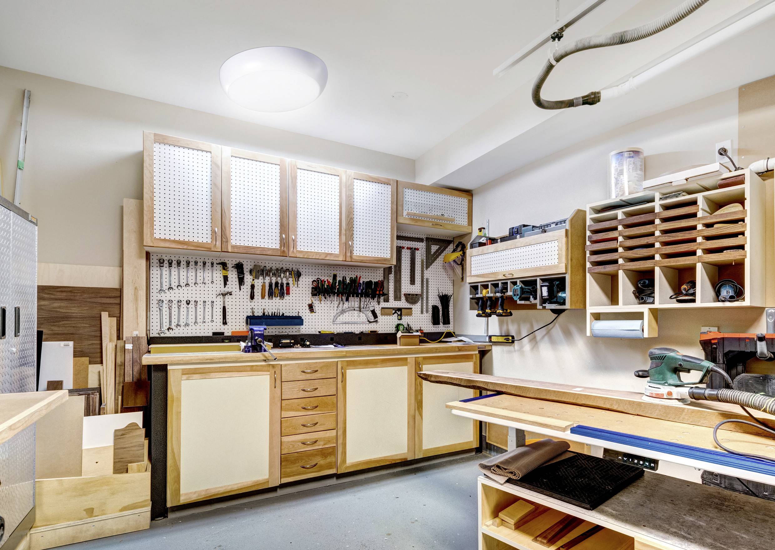 Eine gut organisierte Werkstatt mit Werkzeugen, die an einer Lochplatte hängen, Holzarbeitstischen und Regalen voller Holzbearbeitungsmaterialien.