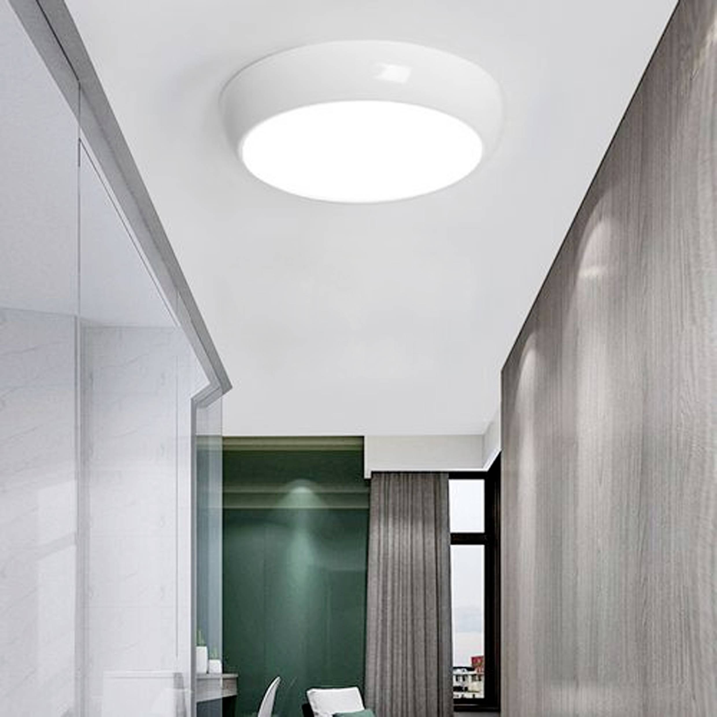 Deckenbeleuchtete kreisförmige LED-Leuchte, die einen modernen Raum mit großen Fenstern und minimalistischer Einrichtung erhellt.