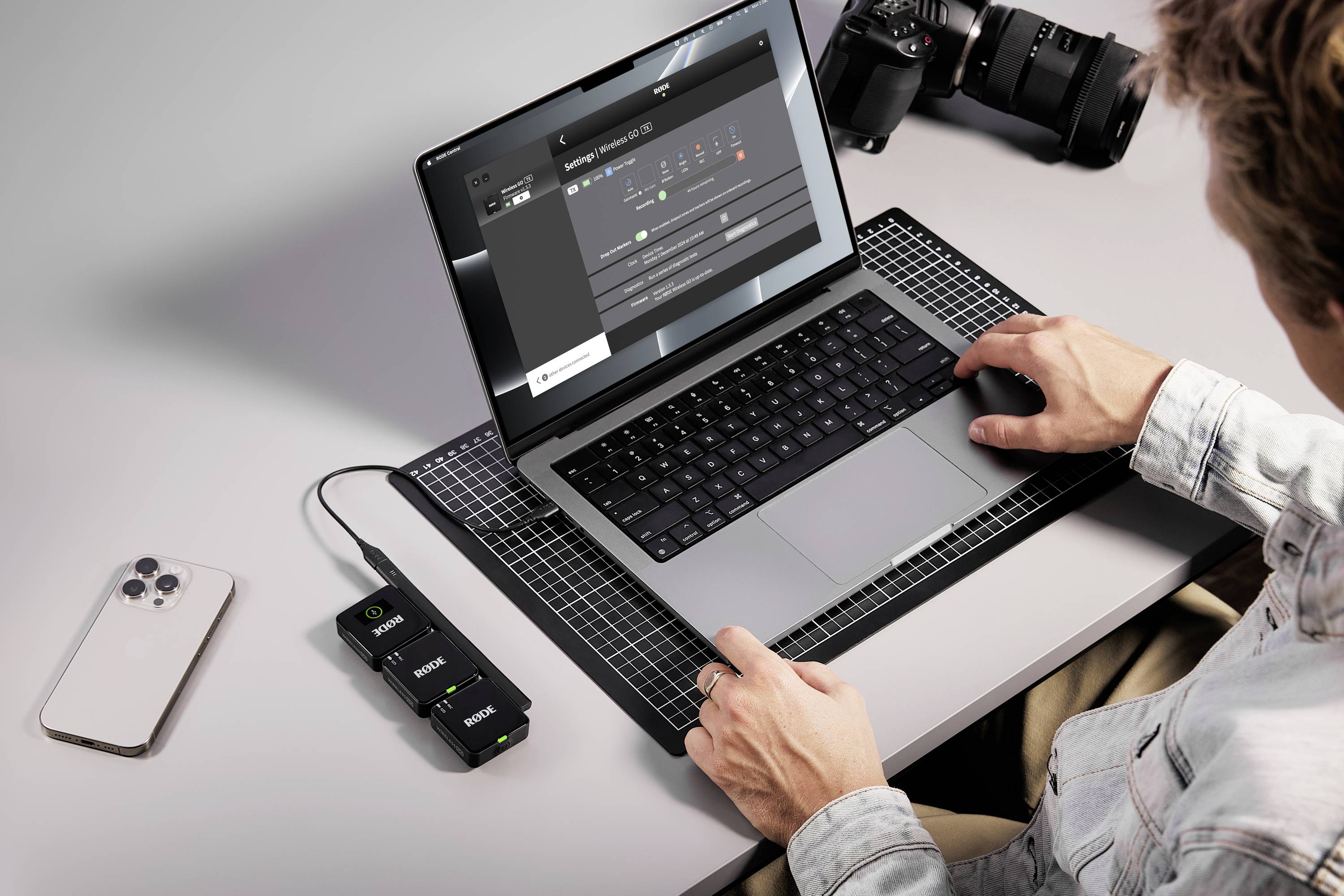 Eine Person arbeitet an einem Laptop mit Bildbearbeitungssoftware. Daneben liegen ein Smartphone, eine Kamera und Akkuladegeräte.
