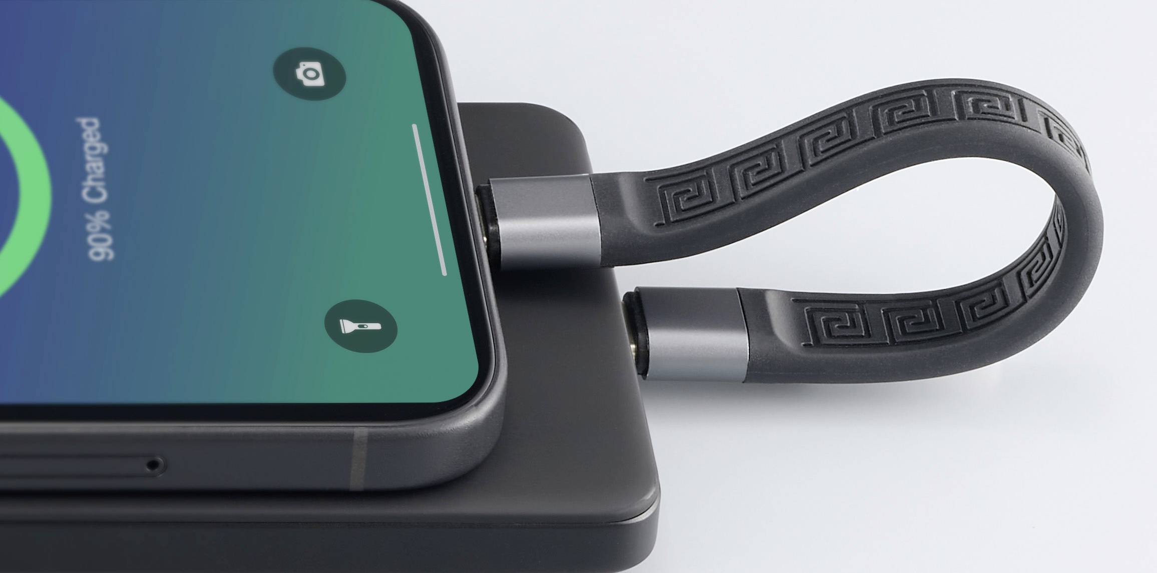 Ein Smartphone mit Ladekabel liegt auf einer Ladematte. Auf dem Bildschirm steht '90% geladen'. Das Kabel hat ein modernes Design.