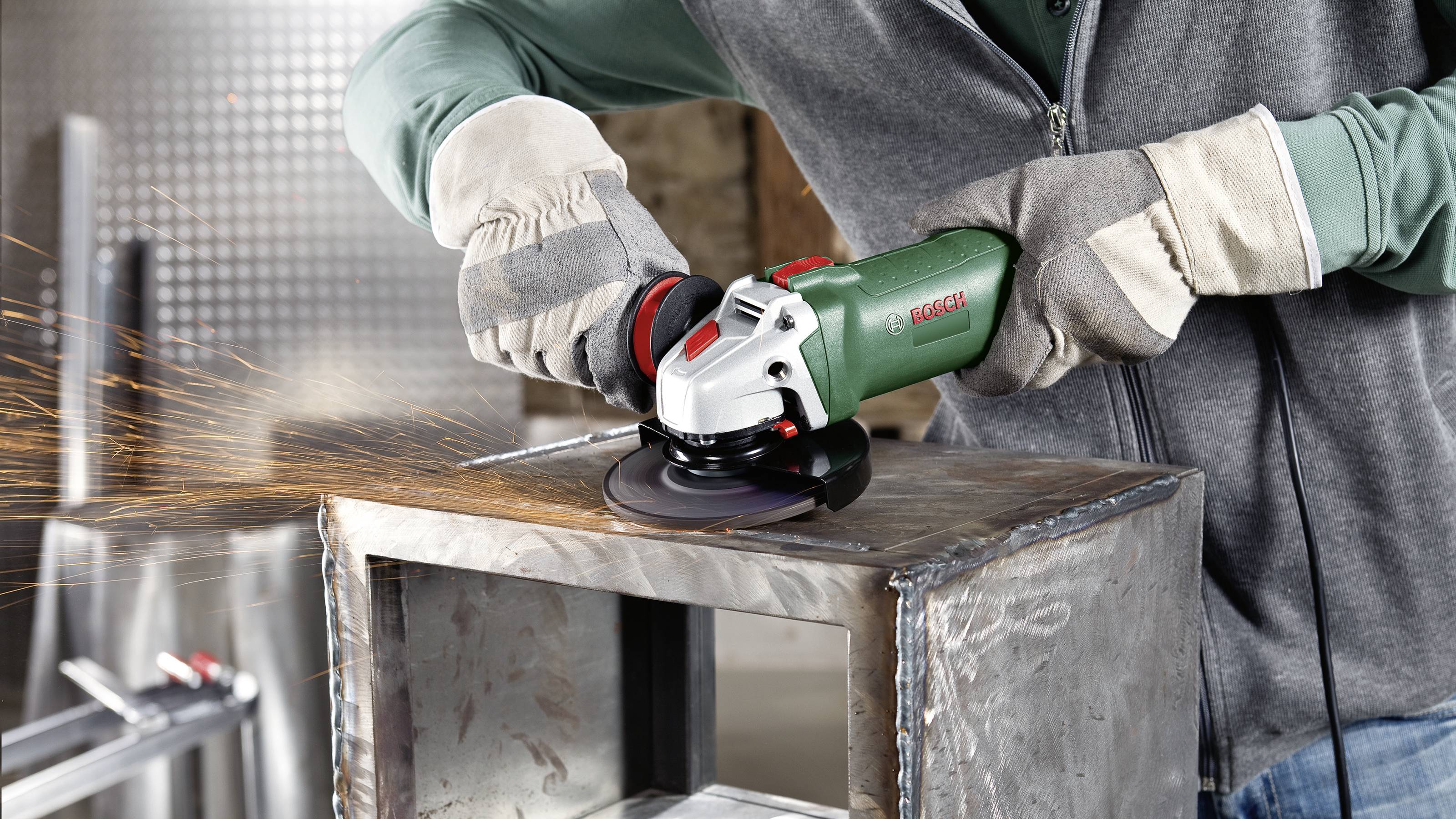 Eine Person trägt Sicherheitsausrüstung und verwendet einen Winkelschleifer, um Metall zu bearbeiten. Funken sprühen während des Schleifens.