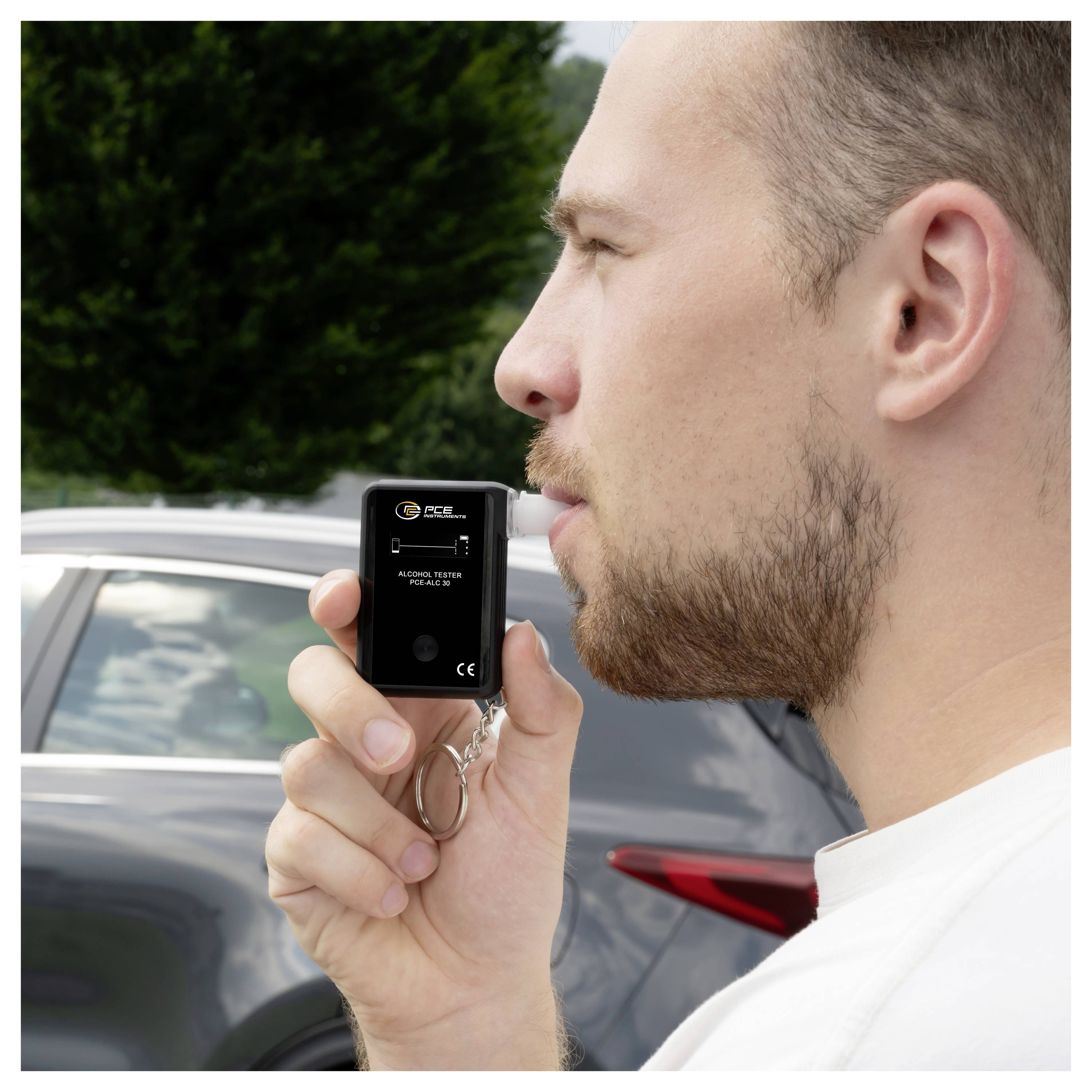 Mann mit einem tragbaren Alkoholtester neben einem geparkten Auto, der seinen Alkoholpegel nach dem Trinken überprüft.