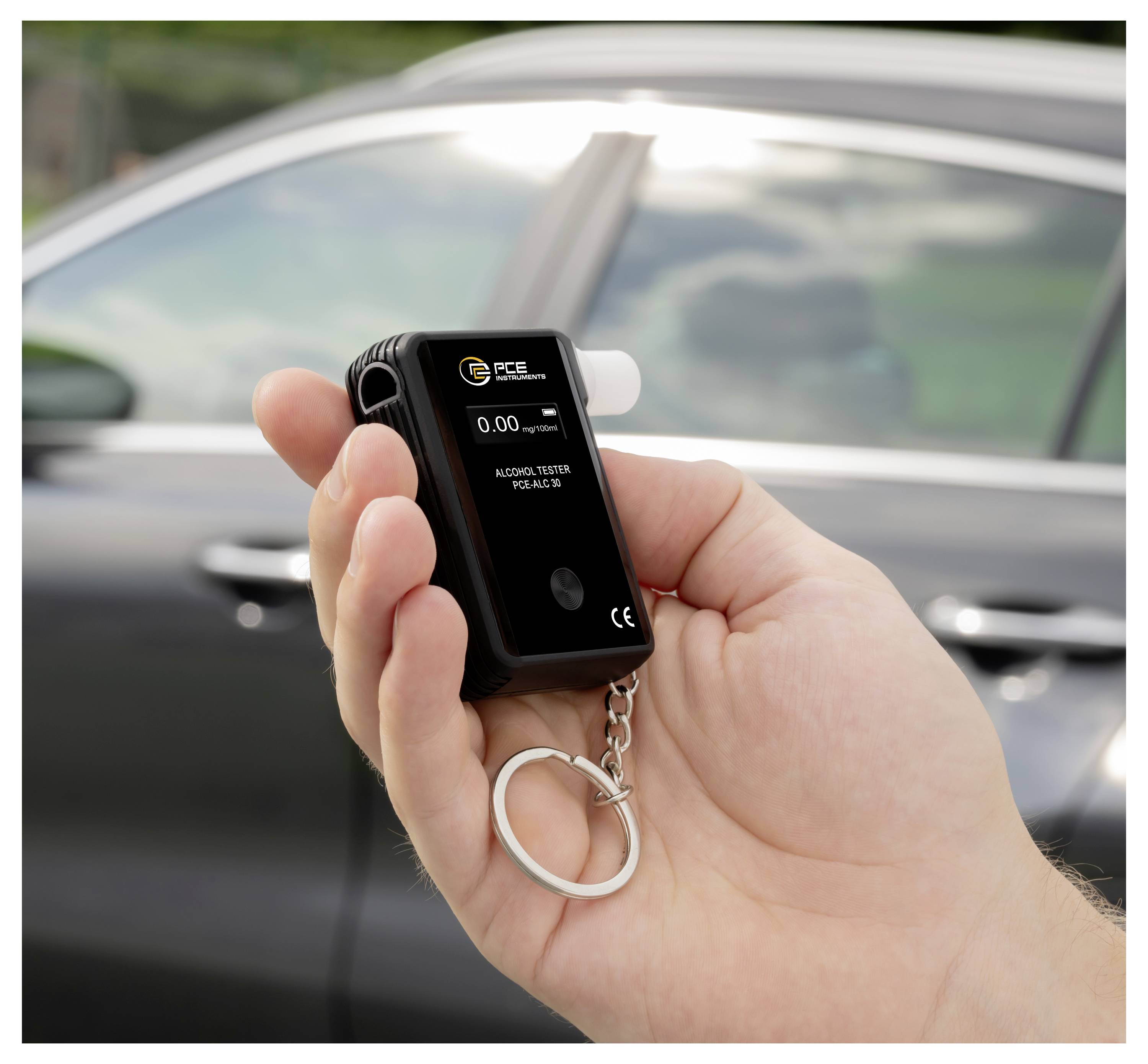 Hand, das einen kompakten Atemalkoholtester-Schlüsselanhänger vor einem Auto hält, zeigt 0.00 auf dem Bildschirm an.