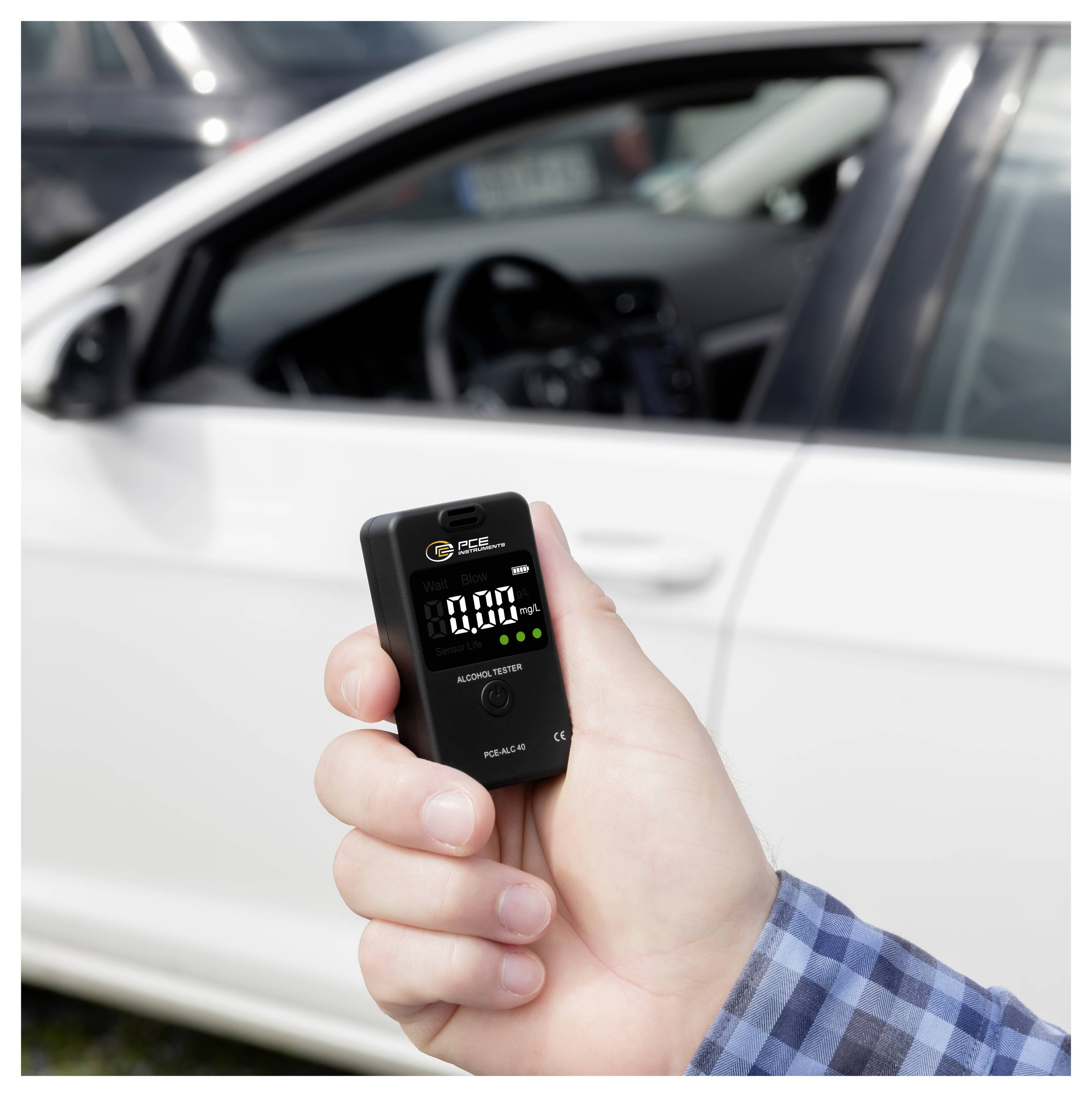 Hand hält ein digitales Atemalkoholtestgerät, das 0,00 anzeigt, vor einem weißen Auto, was eine Nüchternheitskontrolle andeutet.