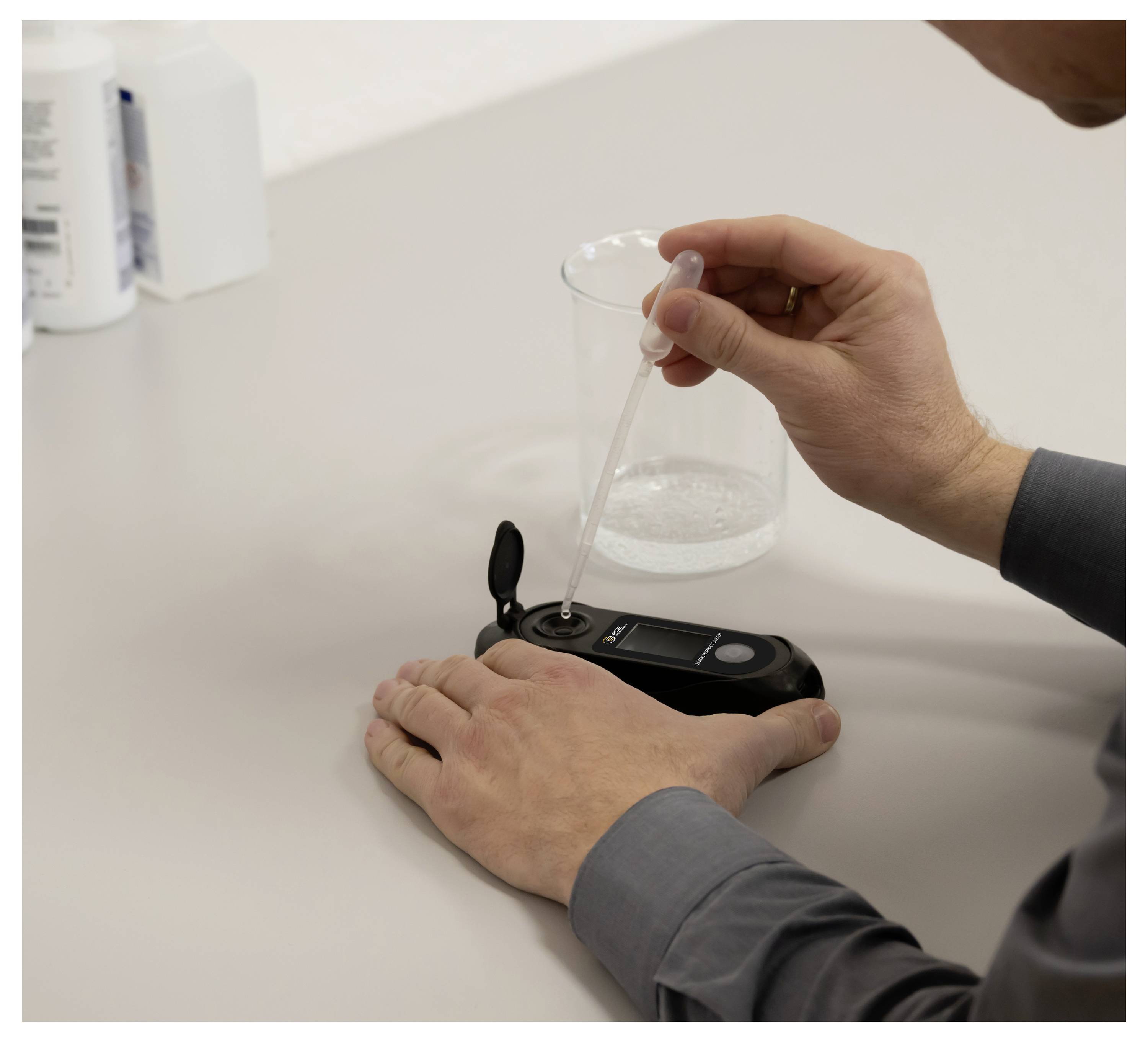 Eine Person verwendet eine Pipette, um Flüssigkeit in ein kleines digitales Testgerät auf einem Labortisch zu geben.