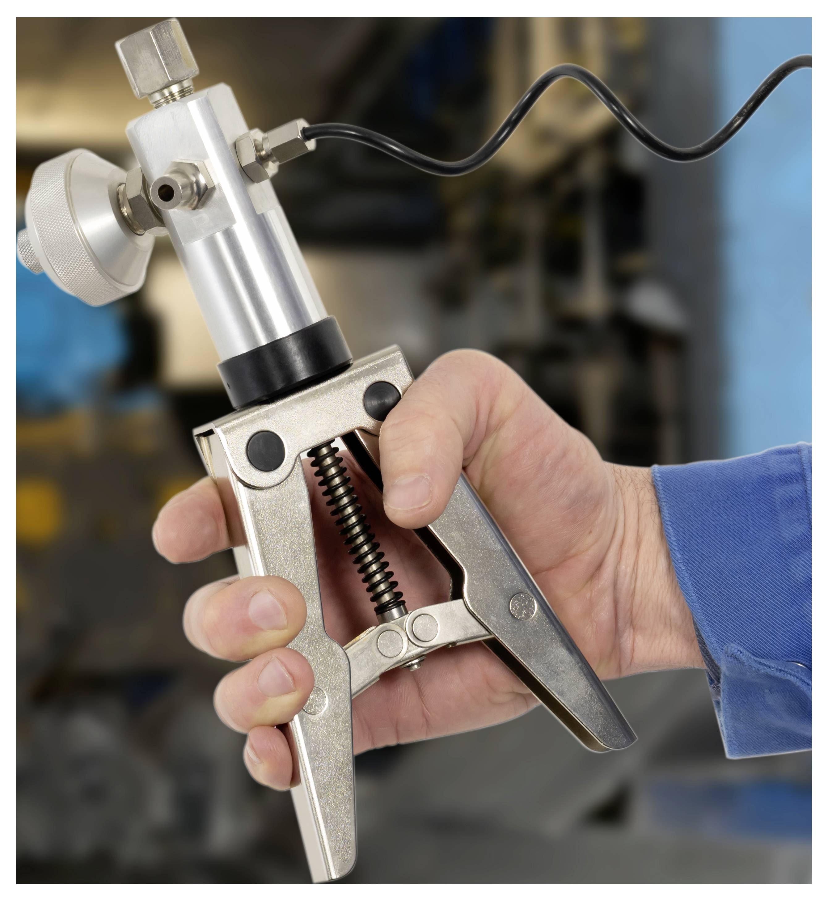 Nahaufnahme einer Hand, die eine metallische federbelastete industrielle Klemme oder ein Werkzeug mit angebrachtem Kabel hält, wahrscheinlich zum Greifen oder Testen verwendet.