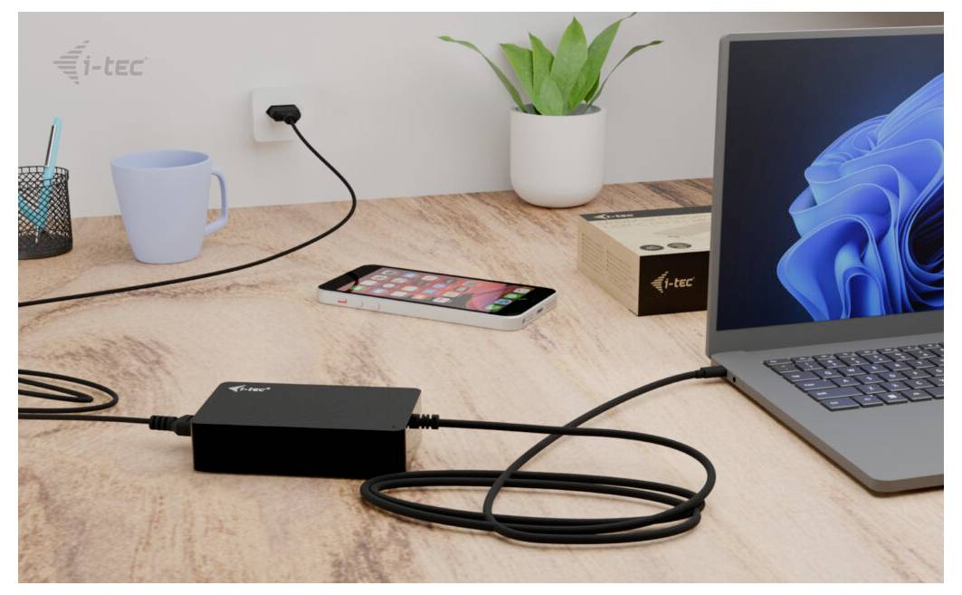 Ein Laptop ist mit einer i-tec Dockingstation verbunden, die auf einem Schreibtisch liegt. Daneben stehen ein Handy, eine Tasse und Pflanzen.