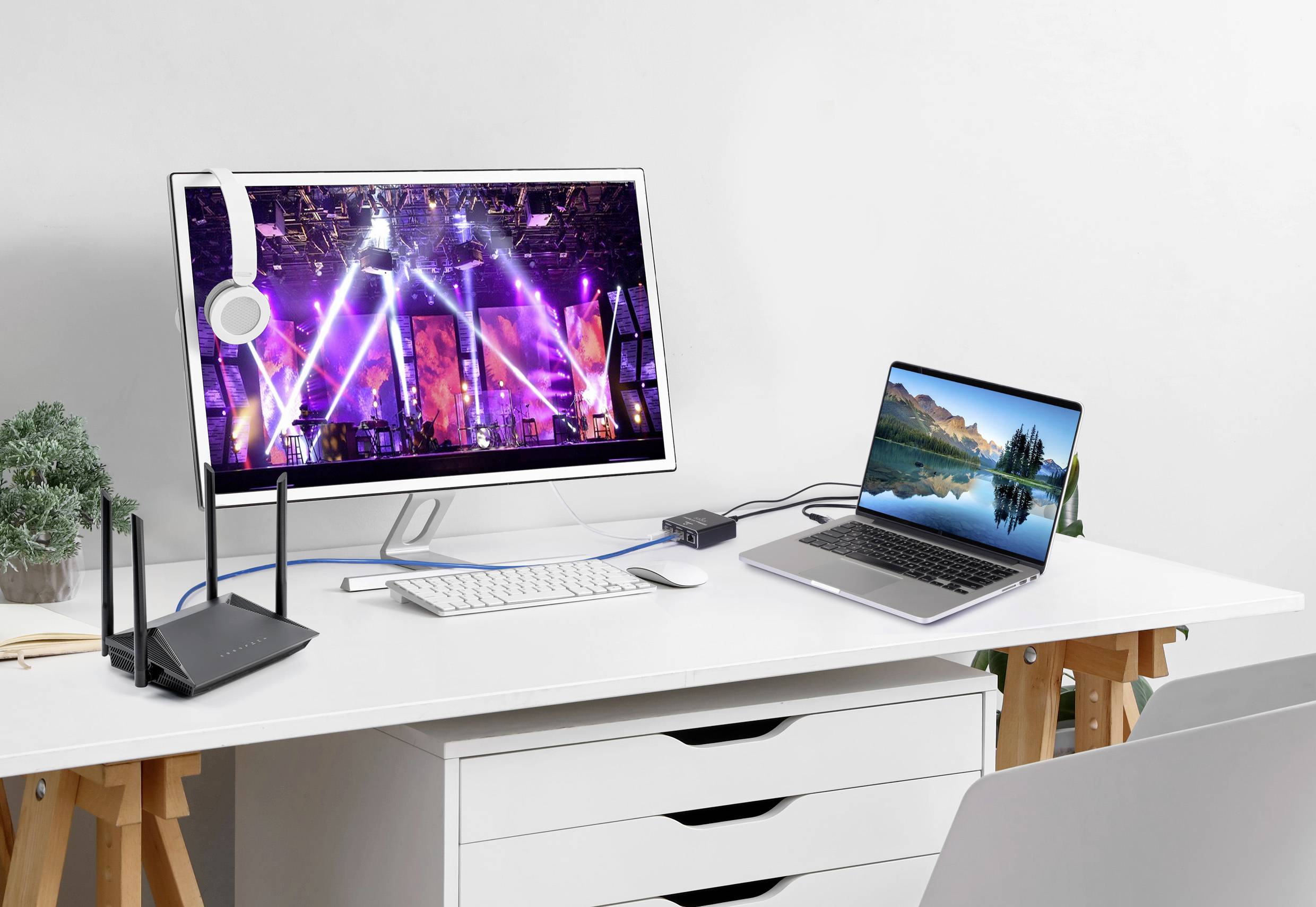 Ein moderner Schreibtisch mit einem Monitor, der eine bunte Bühnenshow zeigt, Laptop mit Naturbildschirm, Tastatur und Router.