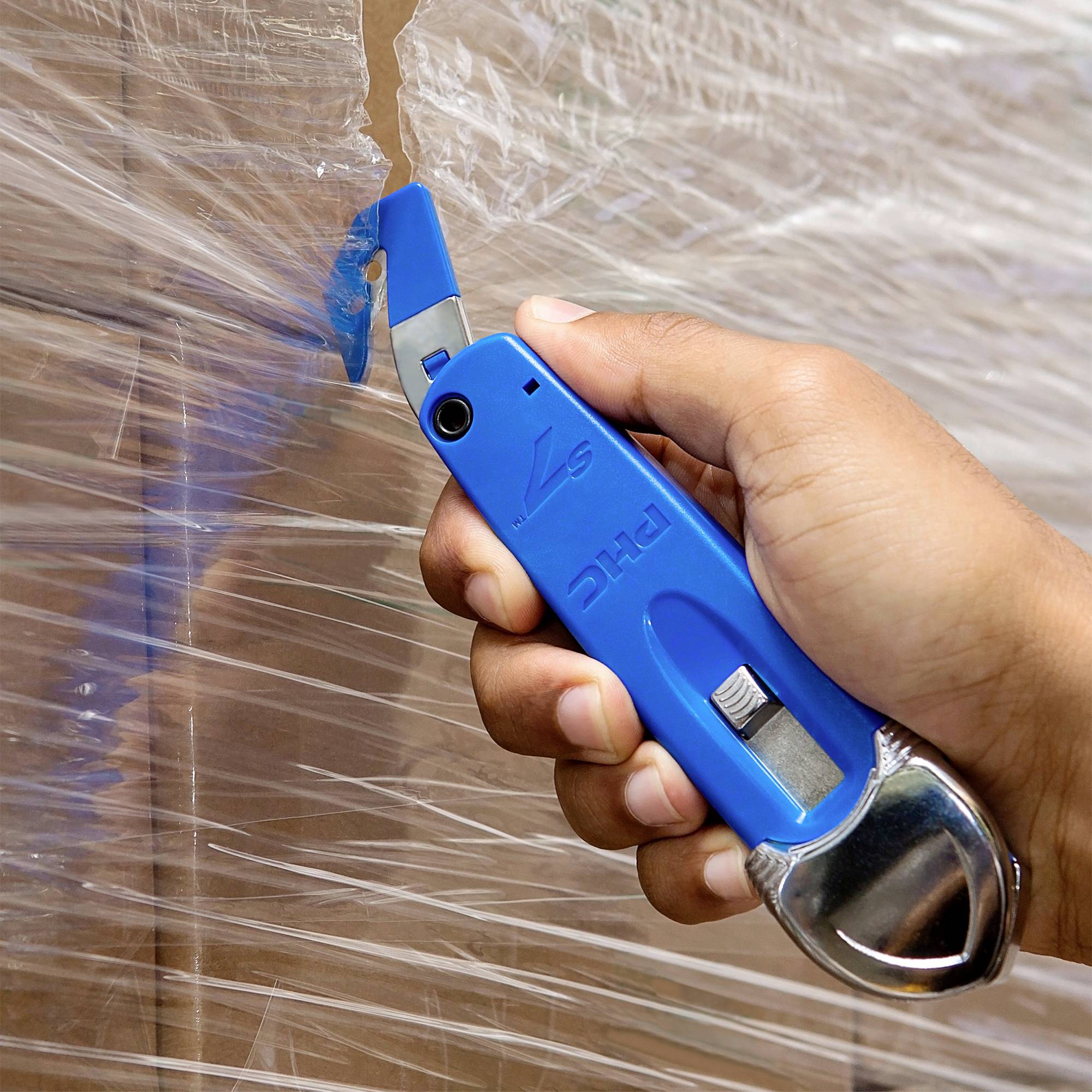 Eine Hand hält ein blaues Sicherheitsmesser, um Verpackungsfolie von einem Karton zu schneiden.