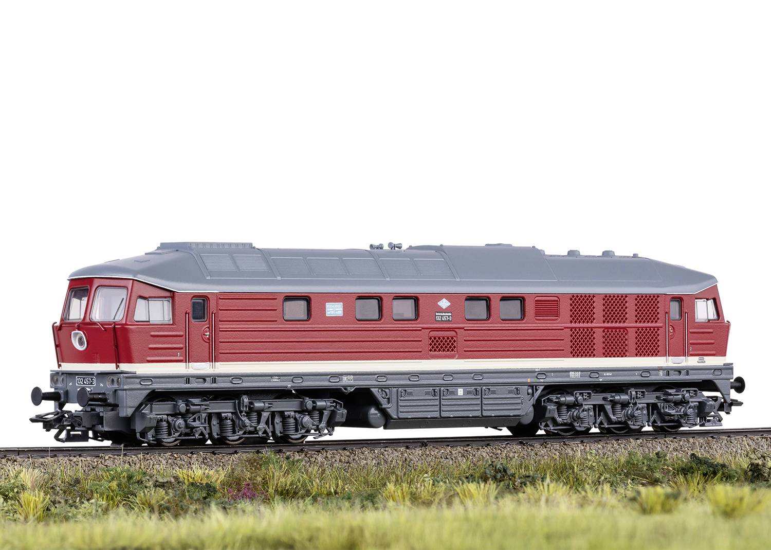 Rotes Modell einer Diesellokomotive auf einem Schienengleis mit einer grün-braunen Wiesenlandschaft im Vordergrund.