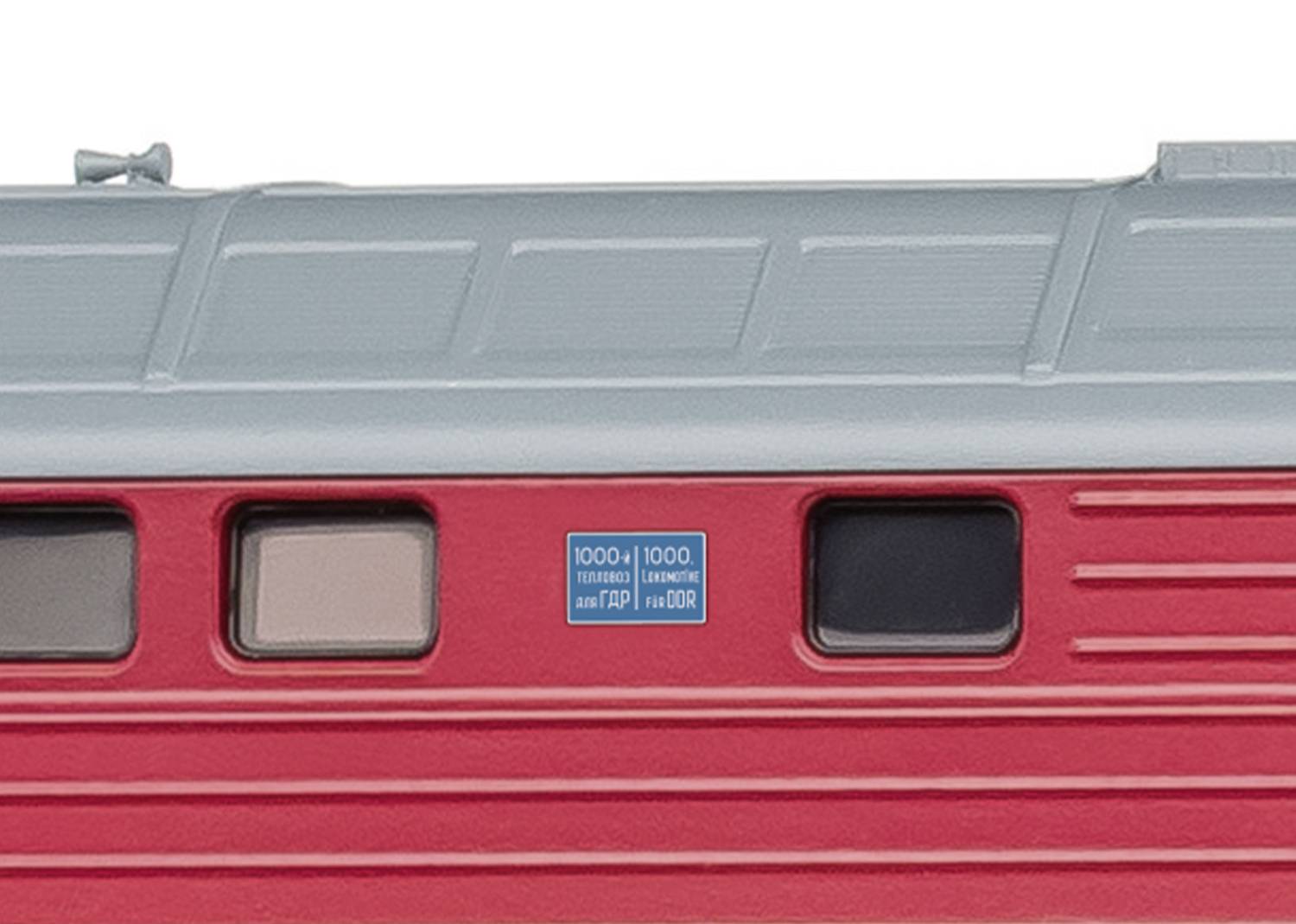 Nahaufnahme eines roten Zugwaggons mit einem blauen Schild und Fenstern. Das Bild zeigt Details einer modernen Zugfassade.