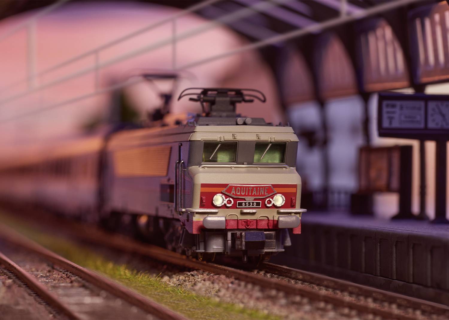 Modellbahn mit detailgetreuem Zug fährt durch eine Miniaturbahnhofsszene. Markante Lok 'Aquitaine' führt den Zug.