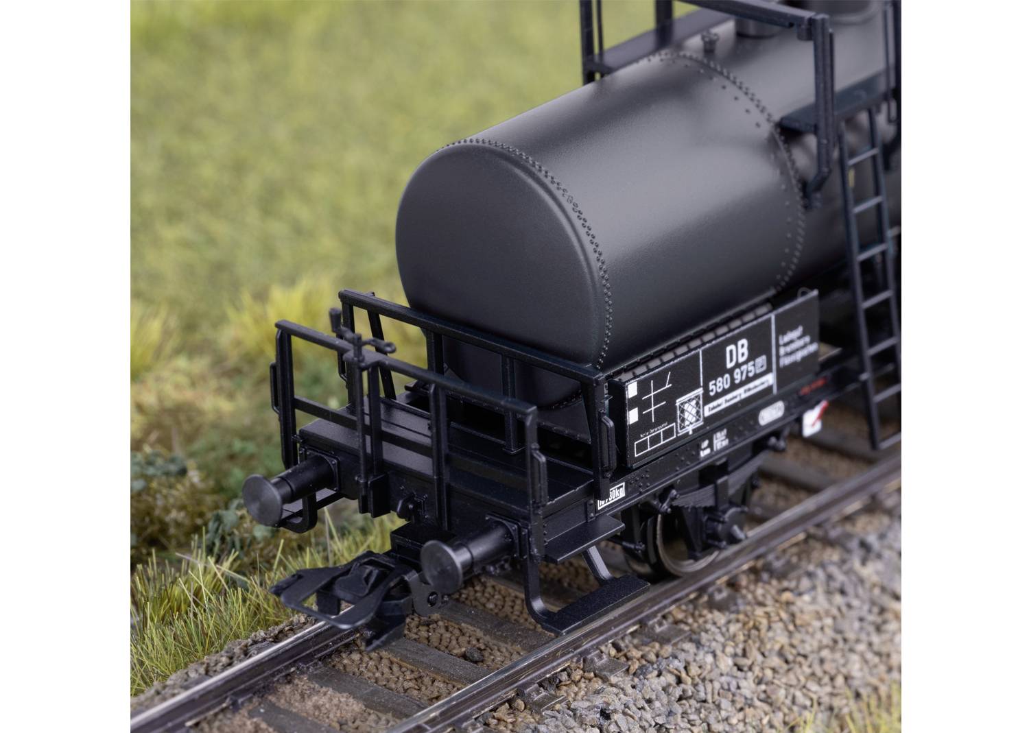 Ein Modell eines grauen Güterwaggons der Deutschen Bahn mit fein detaillierten Schildern und Schienen, umgeben von Gras.