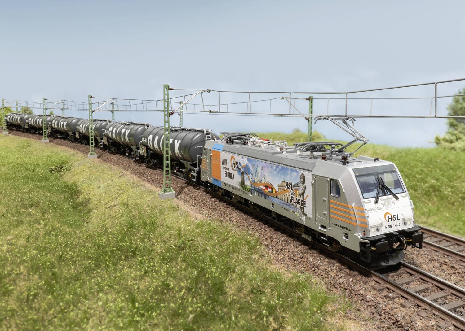 Ein Güterzug fährt auf einer zweigleisigen Strecke durch eine grüne Landschaft. Der Zug besteht aus mehreren Kesselwagen.