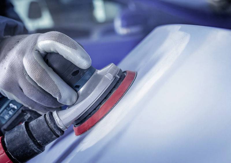 Eine Person poliert eine Autotür mit einer Maschine. Nahaufnahme von Handschuhen und Polierer, Autopflege in einer Werkstatt.