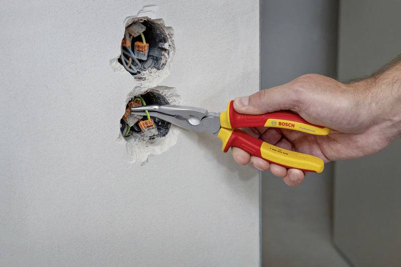 Eine Hand benutzt rote und gelbe Zangenschnittwerkzeuge, um Kabel in einer elektrischen Anschlussdose zu verbinden.