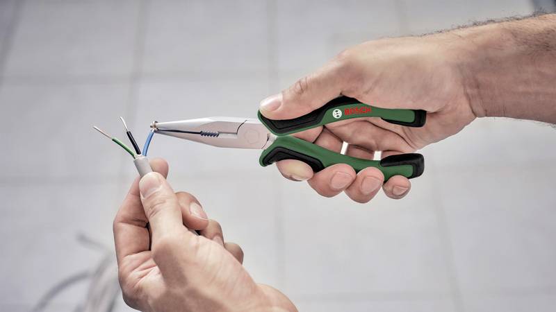 Eine Person hält eine Zange und verbindet Kabel, möglicherweise bei einer elektrischen Arbeit oder Reparatur.