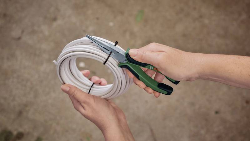 Eine Hand hält eine Zange und schneidet ein weißes Kabel, das von einer anderen Hand gehalten wird.