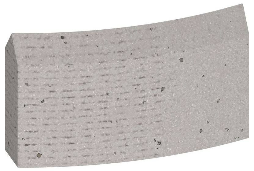Ein grauer, gebogener Betonstein mit rauer Oberfläche und kleinen schwarzen Punkten.