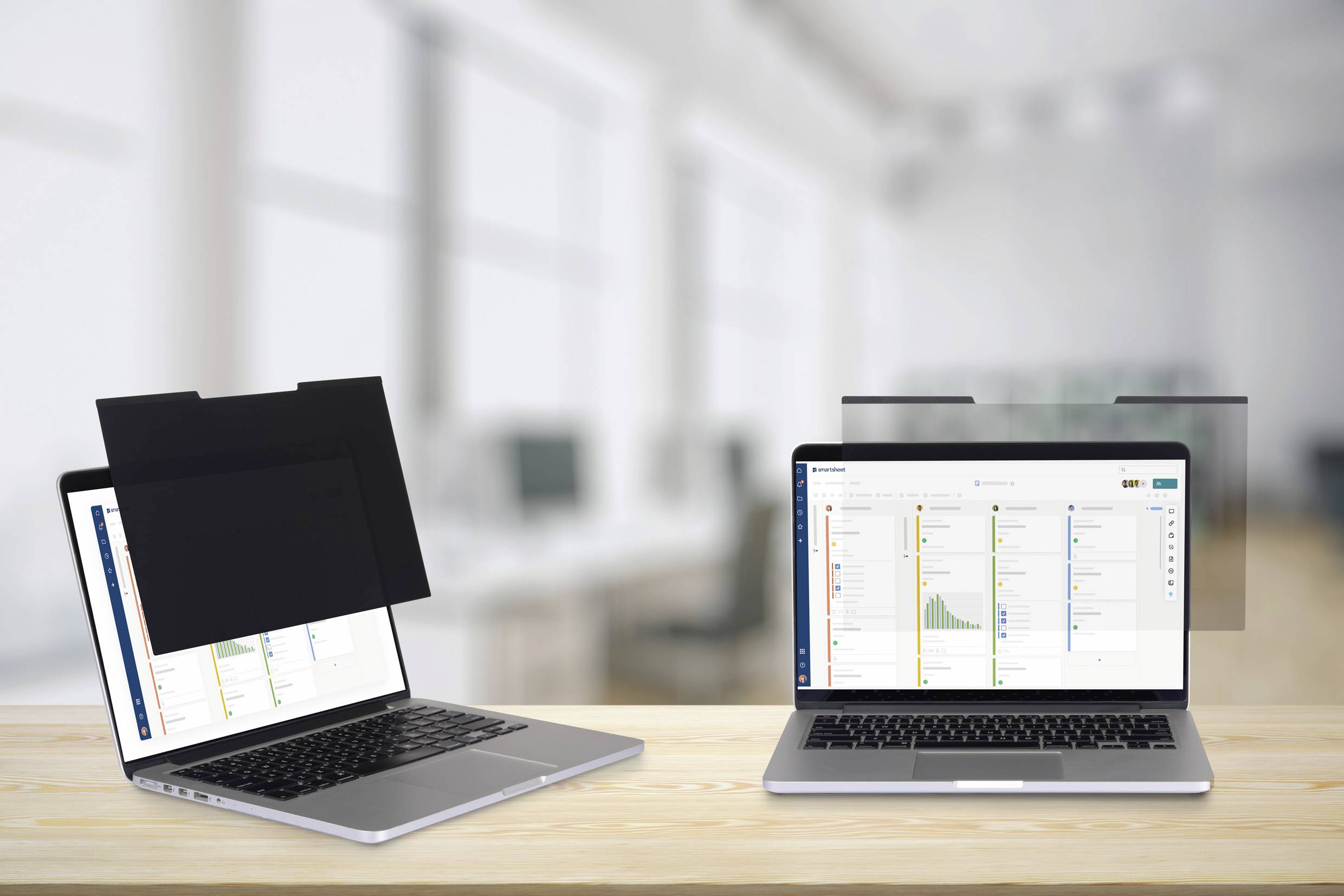Zwei Laptops auf einem Schreibtisch, einer mit einem Blickschutzfilter, der das Display verdunkelt. Büro im Hintergrund unscharf.