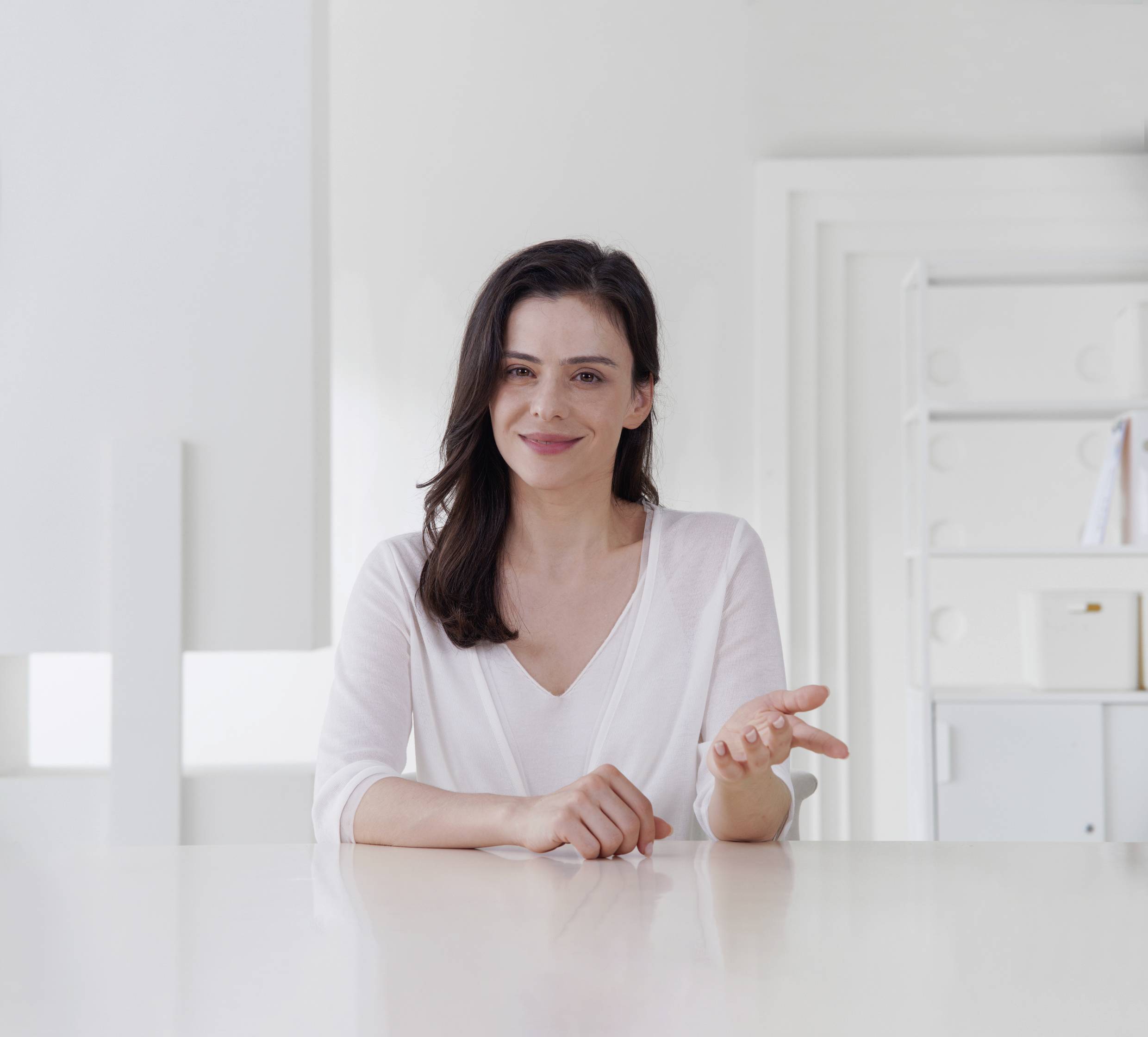 Eine Person sitzt lächelnd an einem Tisch in einem hellen Raum.