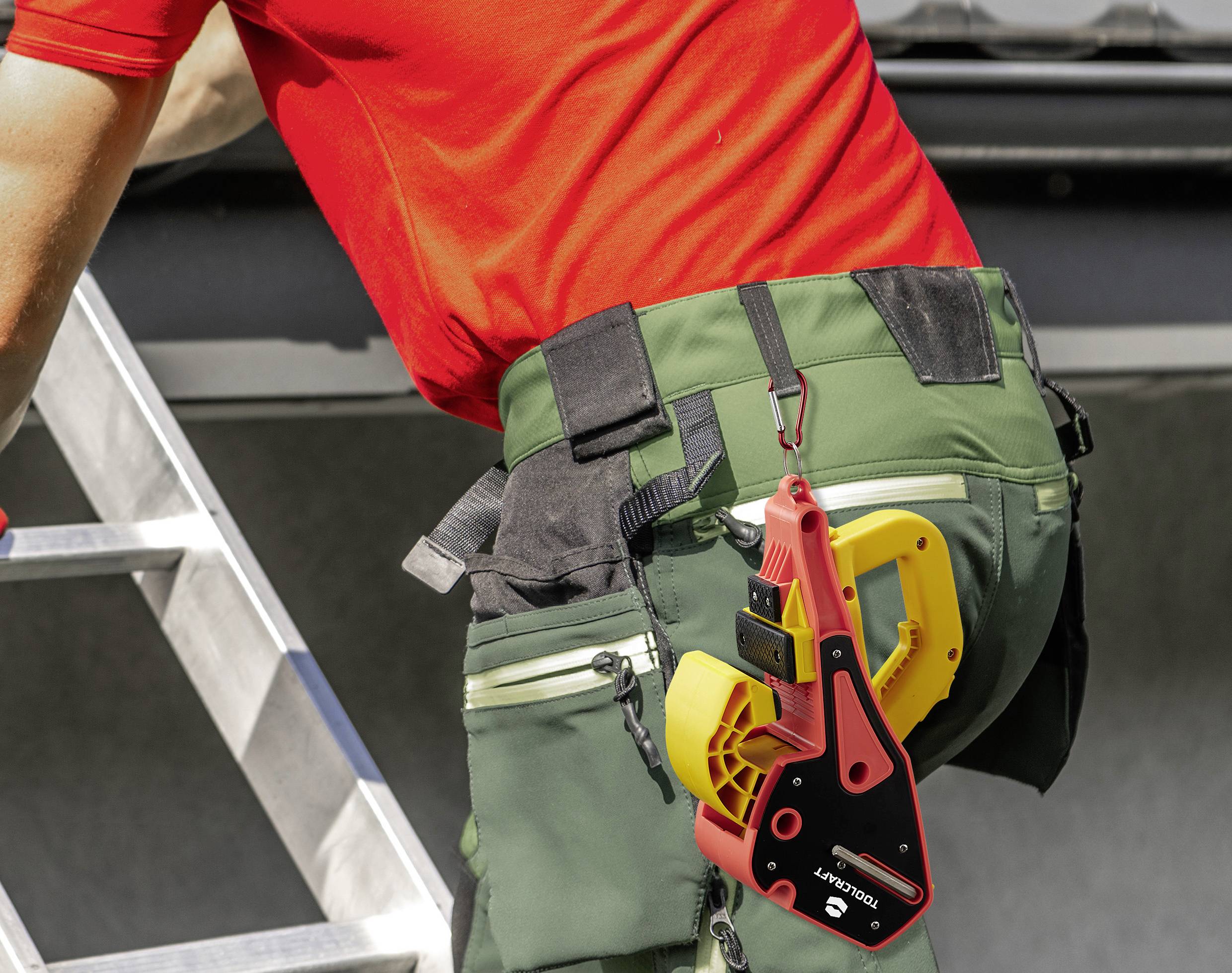 Eine Person im roten T-Shirt und grüner Hose trägt ein Werkzeug an der Hüfte, während sie auf einer Aluminiumleiter steht.
