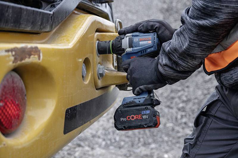 Eine Person verwendet einen Bosch-Akkuschrauber, um eine Schraube an einem gelben Baumaschinenteil festzuziehen.