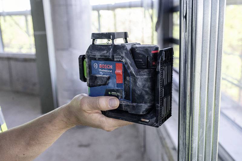 Eine Person hält einen Bosch Professional Laser-Entfernungsmesser in einem Gebäude in der Nähe eines Metallrahmens.