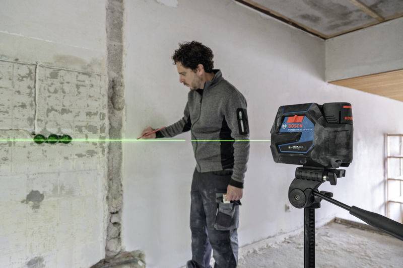 Eine Person nutzt einen Linienlaser beim Renovieren einer Wand, um Präzision sicherzustellen. Der grüne Laserstrahl zeigt eine gerade Linie.