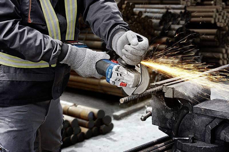 Ein Arbeiter schneidet mit einem Winkelschleifer einen Metallstab. Funken sprühen. Schutzkleidung und Handschuhe werden getragen.