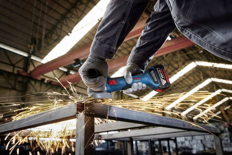 Eine Person schleift Metall mit einem Winkelschleifer. Funken sprühen, während das Gerät die Oberfläche bearbeitet. Die Umgebung wirkt industriell.