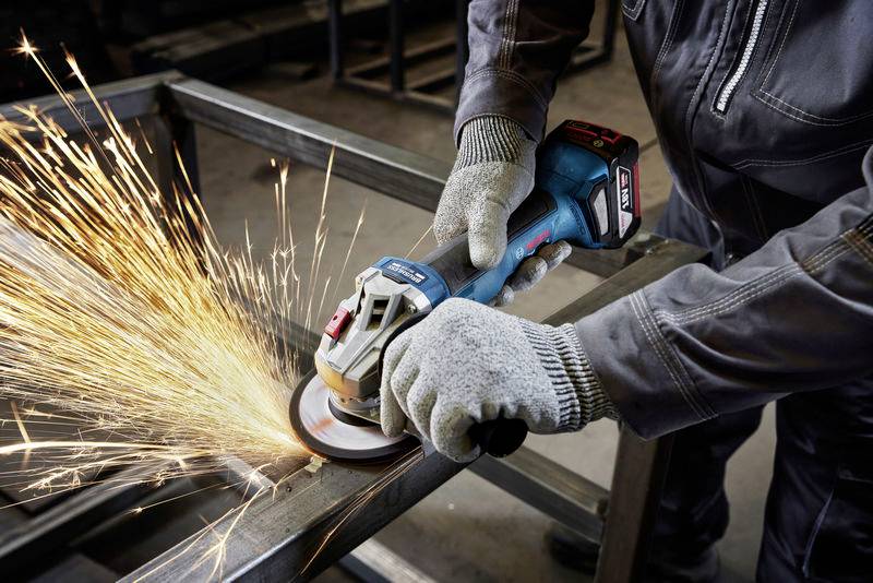 Person verwendet einen Winkelschleifer, um Metall zu bearbeiten, Funken fliegen. Schutzkleidung und Handschuhe werden getragen.