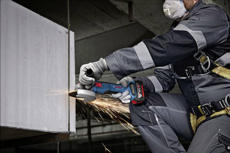 Ein Arbeiter in Schutzkleidung schleift ein Metallstück mit einem Winkelschleifer. Funken fliegen von der geschliffenen Oberfläche.
