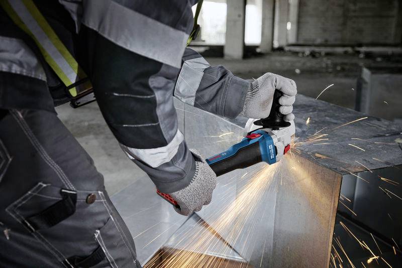 Eine Person in Schutzkleidung schleift mit einem Winkelschleifer Funken von einem Metallstück in einer Werkstattumgebung.