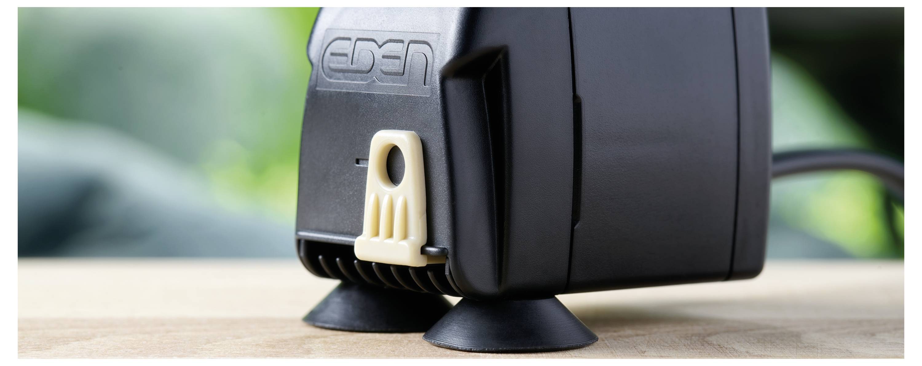 Eine schwarze, kompakte Luftpumpe mit Saugnapfen und einem 'EDEN'-Logo liegt auf einer Holzoberfläche und ist für den Einsatz in Aquarien geeignet.