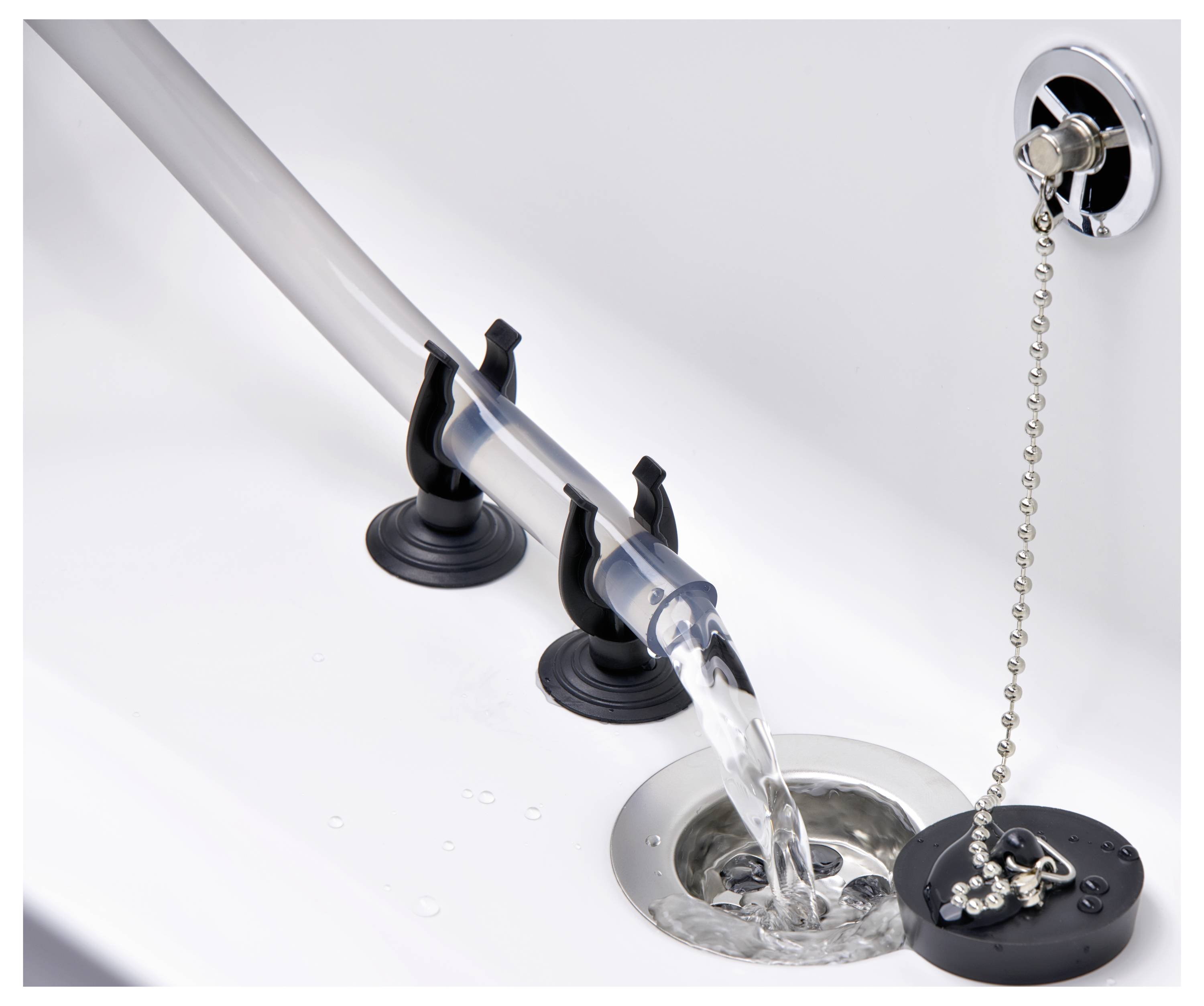 Wasser fließt durch eine transparente Röhre in einen Badewannenablauf, gesichert mit zwei schwarzen Saugnäpfen, während ein Stöpsel mit Kette in der Nähe liegt.