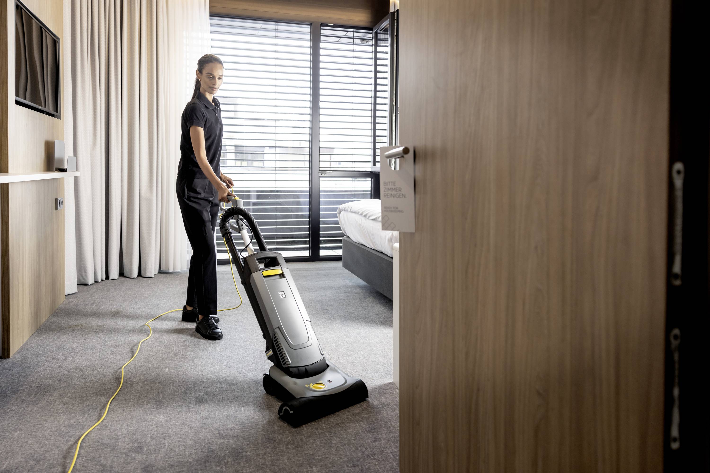 Eine Person saugt mit einem Staubsauger den Teppich in einem modernen Raum mit großem Fenster und Gardinen.