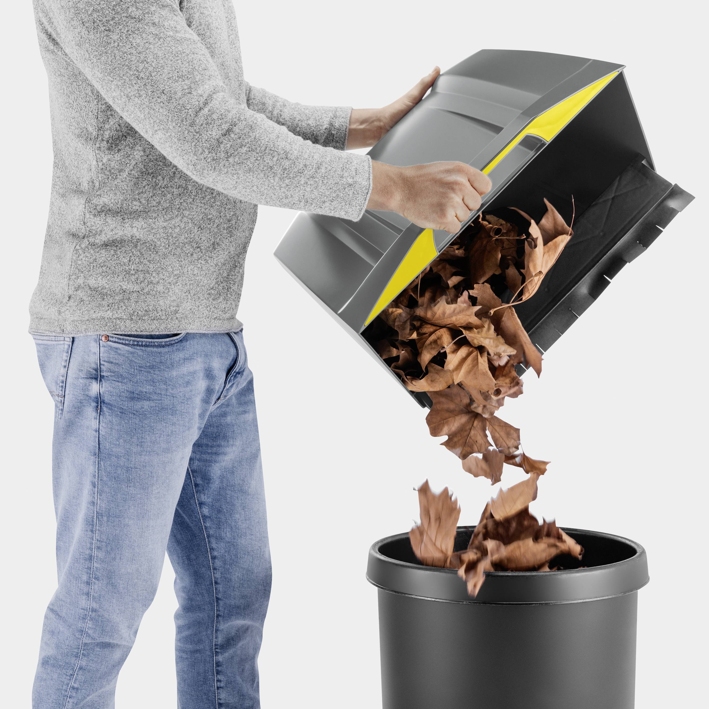 Eine Person leert einen Eimer mit trockenen Blättern in eine schwarze Tonne.