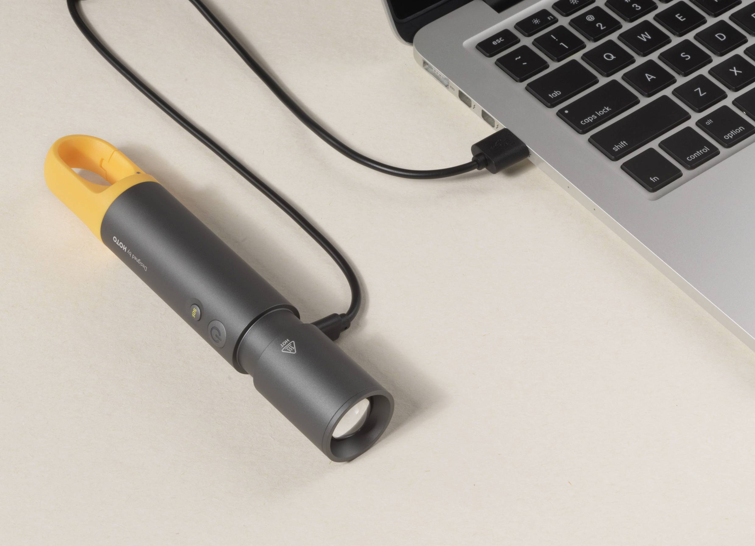 Eine schwarze Taschenlampe mit orangefarbenem Griff ist über ein Kabel mit einem Laptop verbunden.