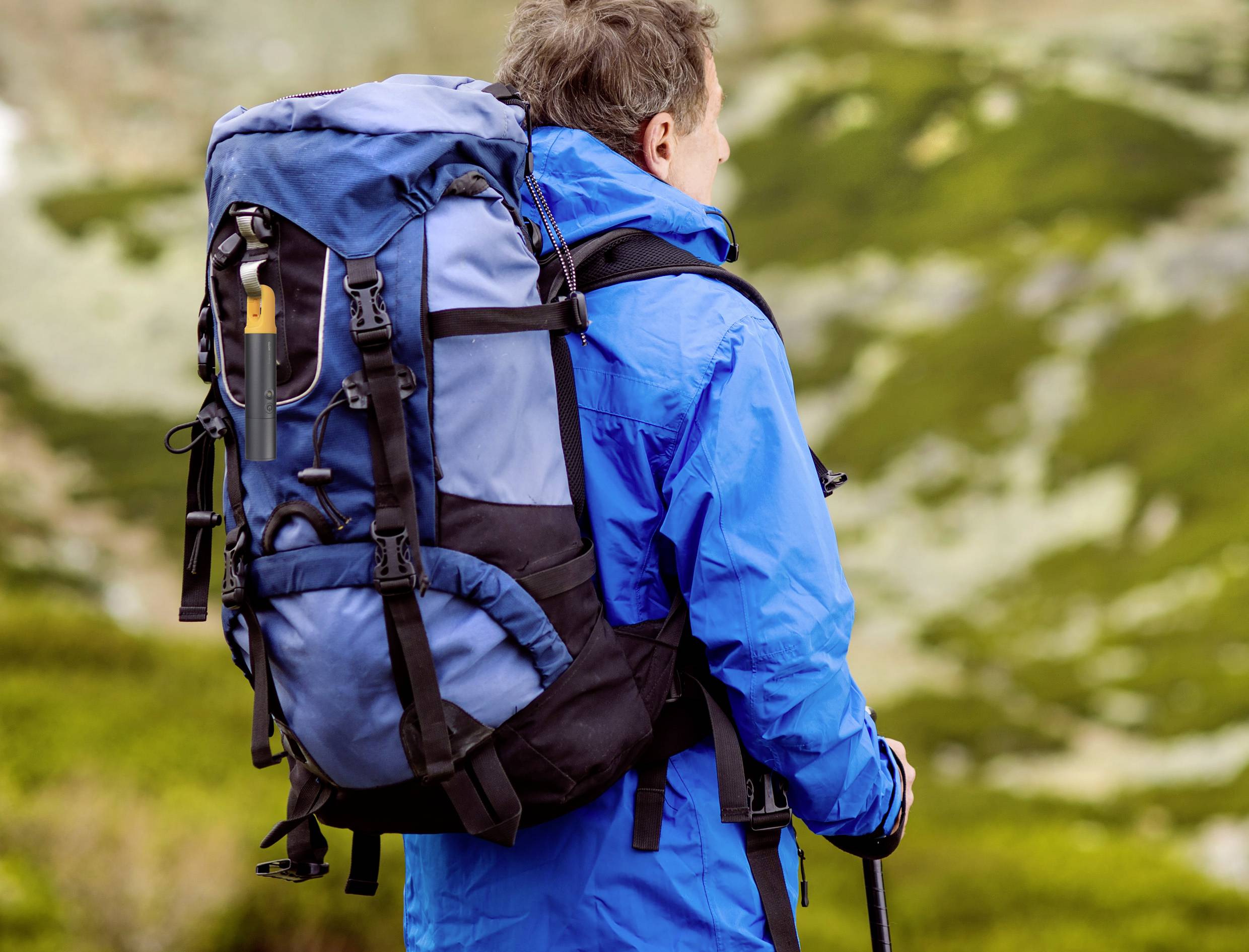 Eine Person in blauer Outdoor-Kleidung mit großem Rucksack blickt in eine bergige Landschaft.