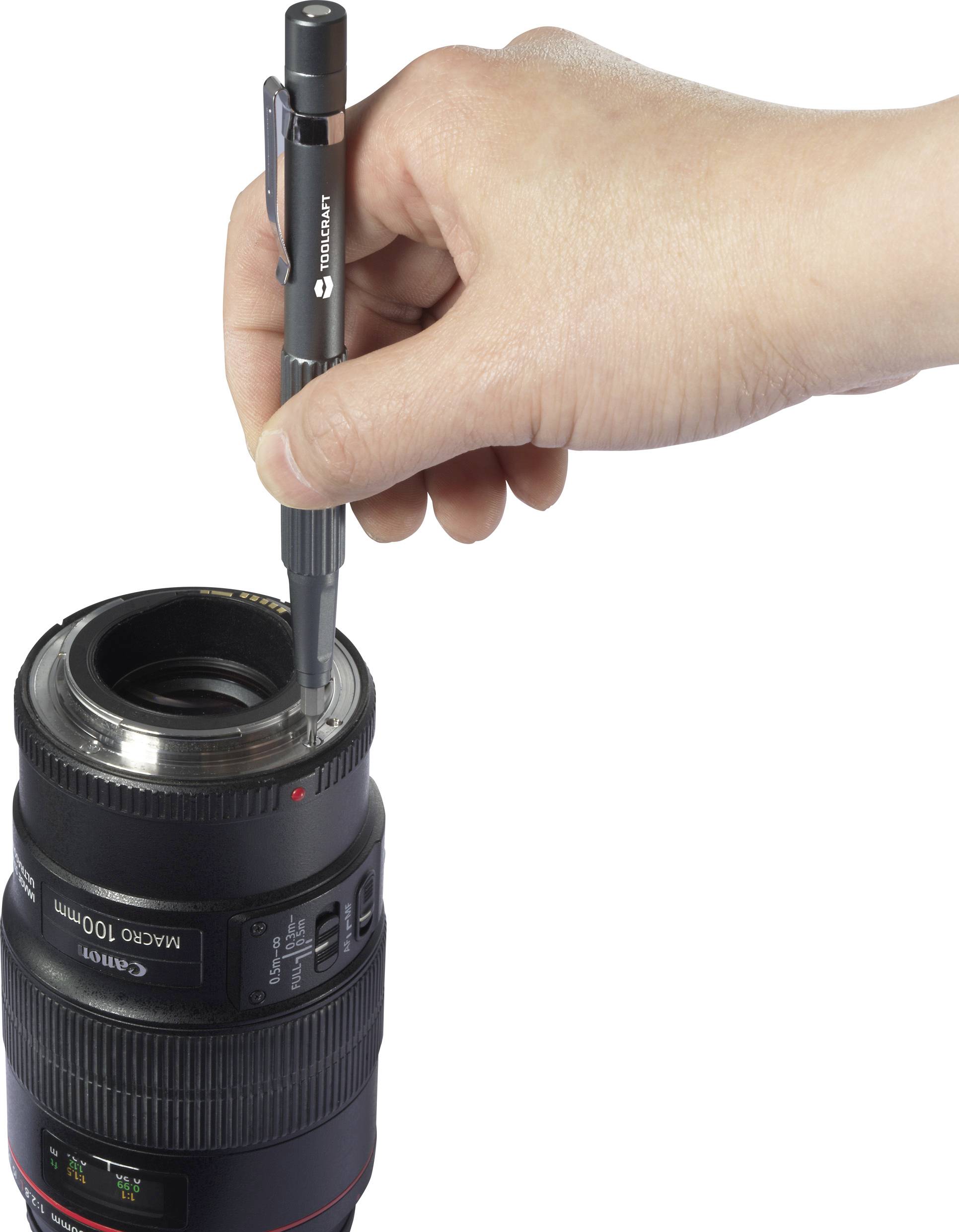 Eine Hand hält einen Stift und dreht damit Schrauben an einem Kameraobjektiv.