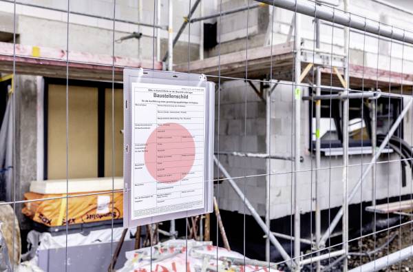 Baugelände mit Sicherheitszaun und Schild 'Baustellenschild', Zeigt Sicherheitsinformationen. Hintergrund: Rohbau eines Gebäudes.