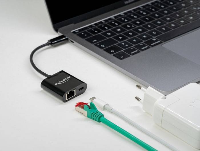 Ein Laptop ist mit einem schwarzen Ethernet-Adapter verbunden. Daneben liegen ein grünes Netzwerkkabel, ein USB-Kabel und ein weißes Netzteil.