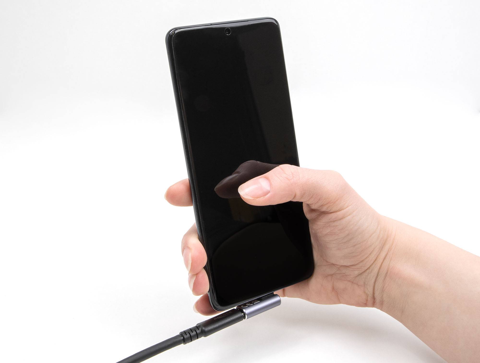 Eine Hand hält ein Smartphone, das mit einem Ladekabel verbunden ist. Der Bildschirm ist schwarz und das Gerät ist nicht eingeschaltet.