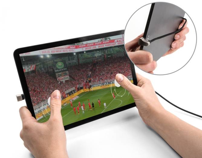 Eine Person hält ein Tablet, auf dem ein Fußballspiel mit einem Freistoß zu sehen ist. Das Tablet ist über ein Kabel verbunden.