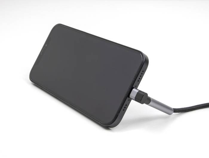 Ein schwarzes Smartphone liegt auf einem Tisch und wird über ein USB-Kabel aufgeladen. Das Display ist ausgeschaltet.