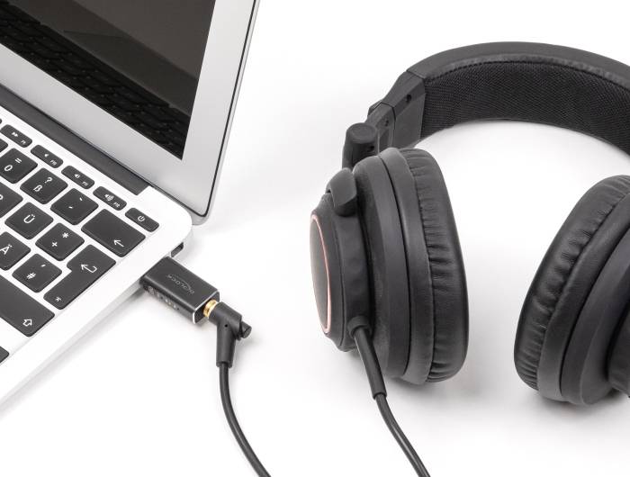 Laptop mit angeschlossenen Over-Ear-Kopfhörern, die seitlich auf einer Tischplatte liegen.